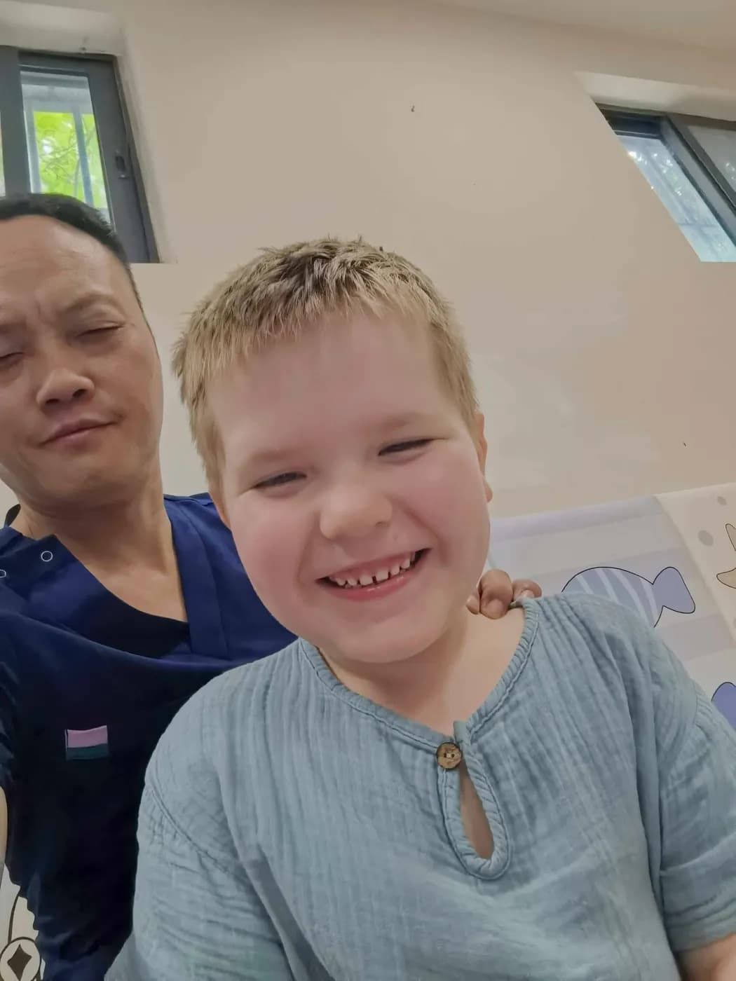 雷静波——与微笑的男孩患者合影，旁边是画着鱼和海星的儿童装饰板