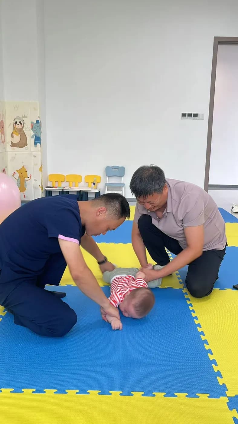 两名男子在诊室内帮助一名小患者趴在爬行垫上
