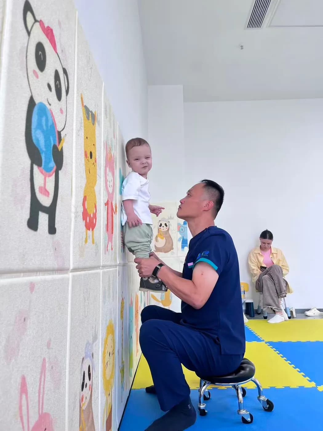 一名男子抱着幼儿站在画有卡通形象的墙边