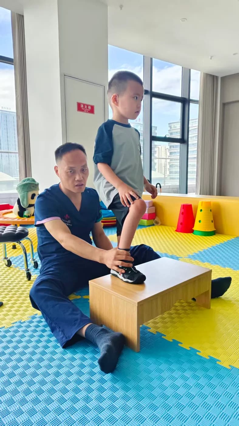 一名穿医疗服的男子用手扶住男孩踩在木质踏台上的脚