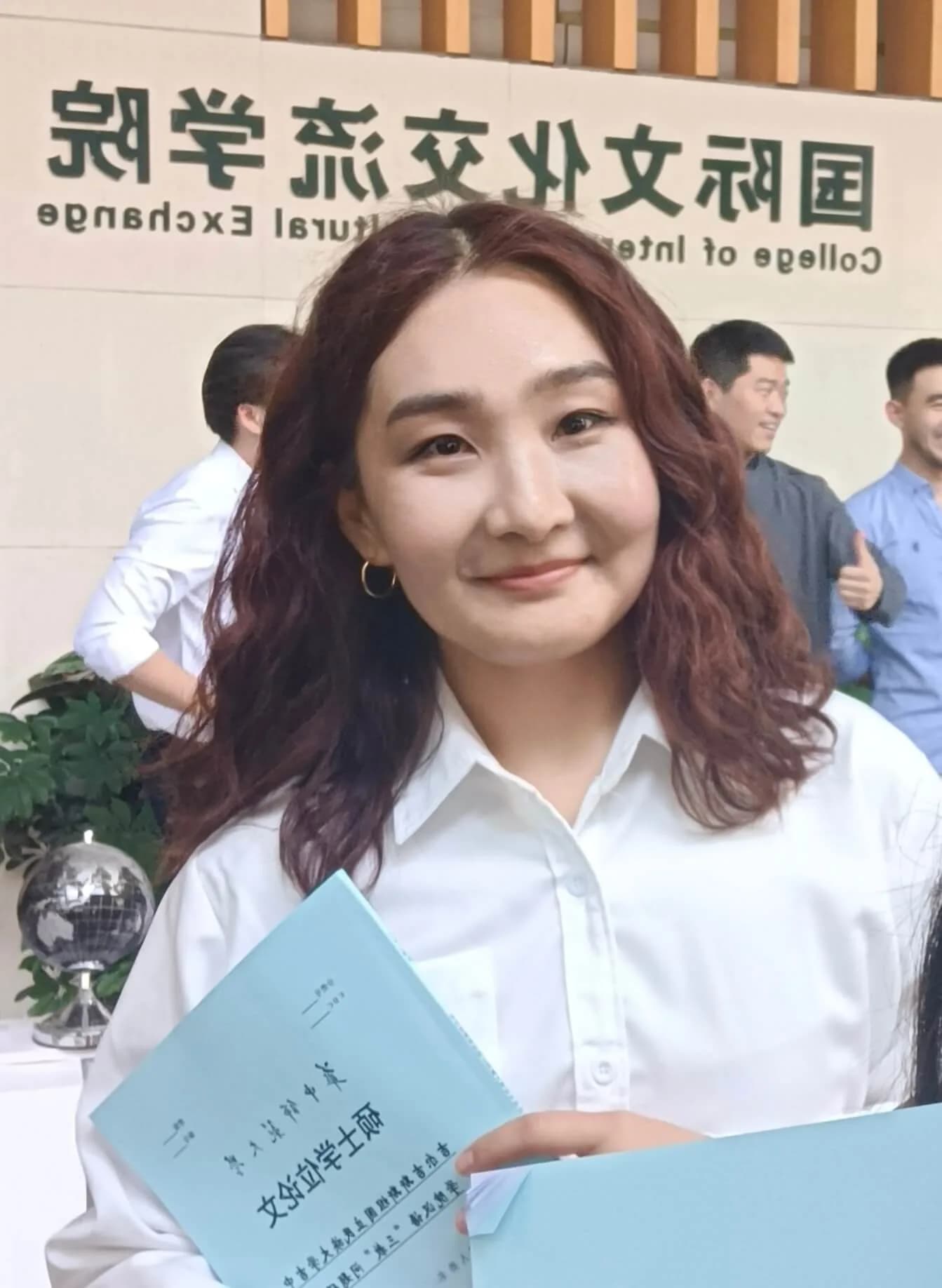Musaeva Gaukhar 手持毕业证书，身后墙面上有院校标牌
